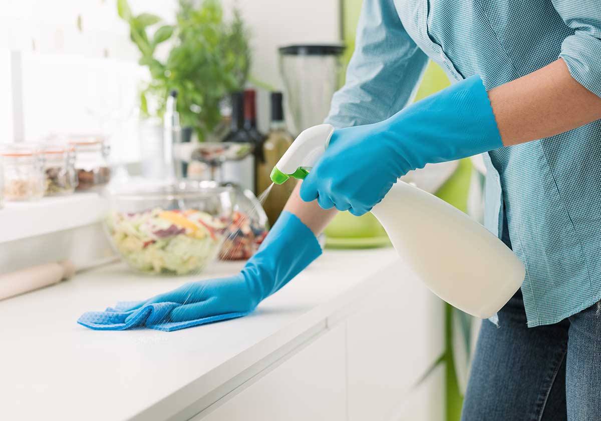 Woman using rag and sprayer for cleaning table with colleagues i